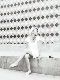 Happy young woman sitting against wall