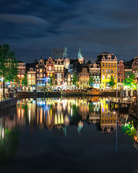 Illuminated buildings by lake against sky in city at night