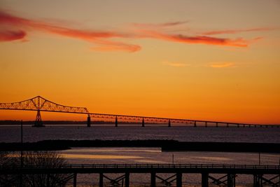 Silhouette bridge over sea against sky during sunset