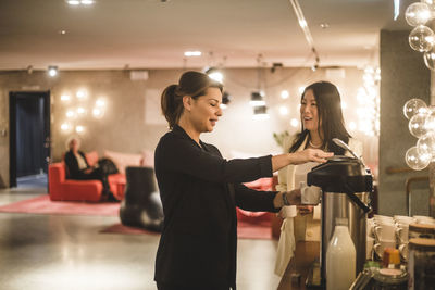 Female coworkers talking while standing by coffee maker in creative office