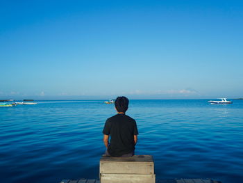 Rear view of boy sitting at beach against sky