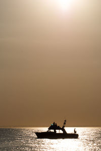 Silhouette people in sea against sky during sunset