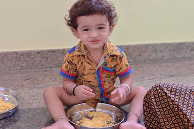 A child sits inside the house eating food and the little boy has a plate full of food