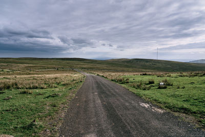 Road passing through field against sky