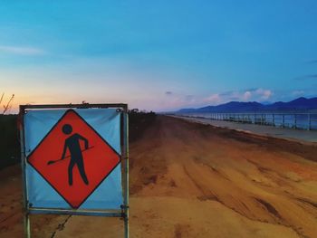 Road sign on beach against sky during sunset