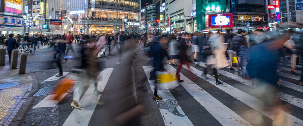 Blurred motion of crowd walking on illuminated city at night