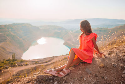 Rear view of woman sitting on mountain against sky