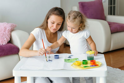 Mother and toddler daughter painting at home. happy creative family with child spending time