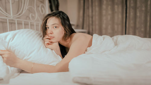 Portrait of young woman lying on bed at home