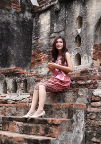 Portrait of woman sitting against brick wall