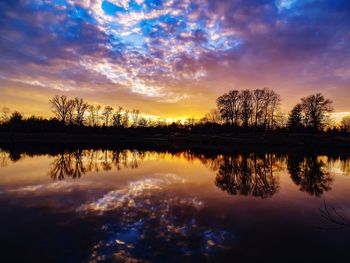 Reflection of silhouette trees in lake against sky during sunset