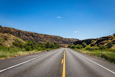 Empty road by mountain against blue sky