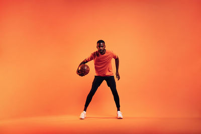 Man with basketball standing against orange background