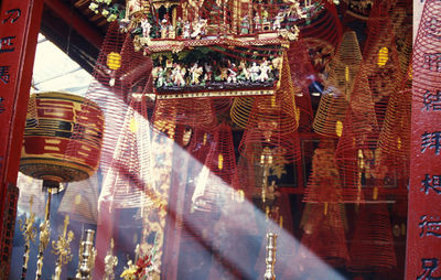 Low angle view of sunlight streaming by spiral incense sticks hanging in temple