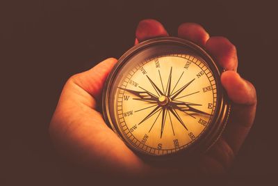 Cropped hand of person holding navigational compass against black background