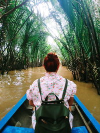 Rear view of woman sitting amidst trees in boat on canal