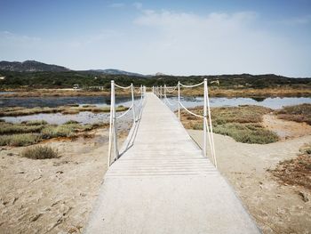 Wooden footbridge leading towards water against sky