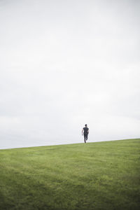 Mid distance view of young man running on field against sky