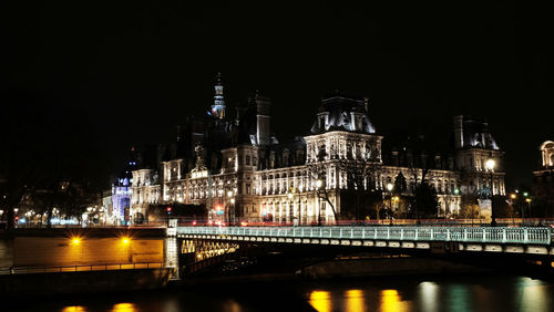 Illuminated bridge over river against sky at night