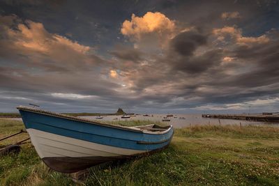 Boat moored on field by sea against cloudy sky