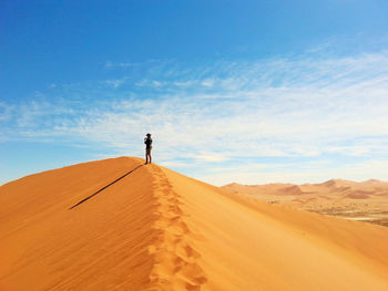 Man standing on sand dune in desert against sky