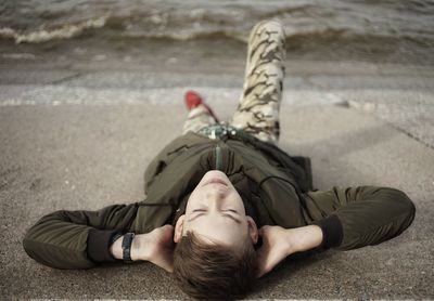 High angle view of teenage boy lying on footpath by sea
