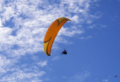 Low angle view of people paragliding against blue sky