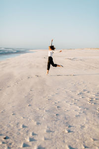 Man jumping on beach against clear sky