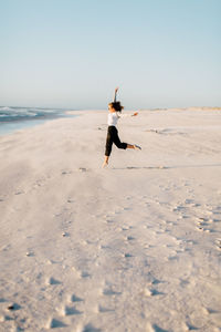 Young woman jumping at beach against clear sky during sunset