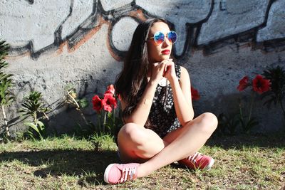 Young woman sitting on wall by plants