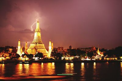 Illuminated wat arun by river against cloudy sky at dusk