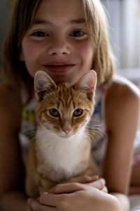 Portrait of smiling girl sitting with cat on bed at home
