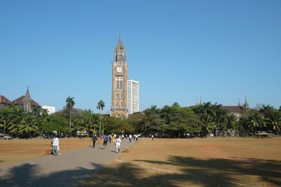 People in park by buildings against clear blue sky