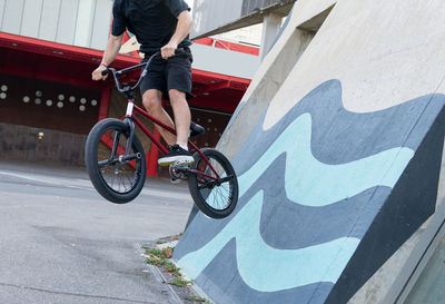 Side view of cropped unrecognizable young male in casual clothes riding concrete wall on bmx bicycle while spending time in skate park in weekend