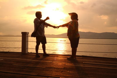 Full length of silhouette friends standing by sea against sky during sunset