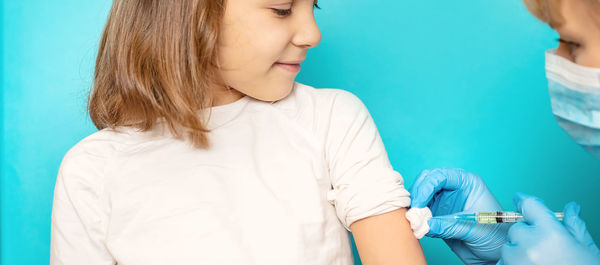 Doctor giving vaccine to girl against blue background