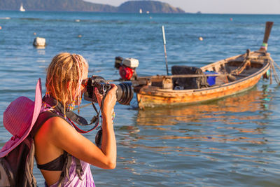 Side view of woman photographing boat in sea