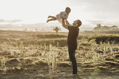 Father playing with young girl at beach during sunset