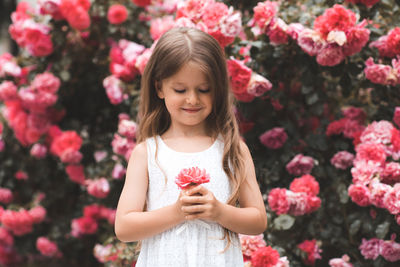 Cute baby girl 5-6 year old hold rose flower sit over bloom bushes in garden outdoor. spring season