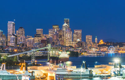 Illuminated buildings in city against clear blue sky