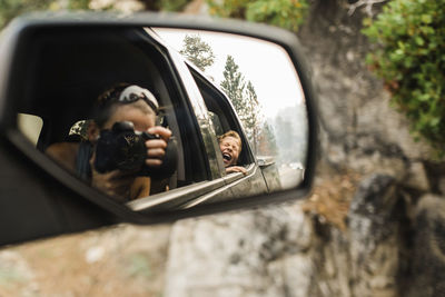 Son screaming while mother photographing with camera reflecting on side-view mirror