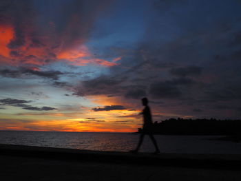 Silhouette man by sea against sky during sunset