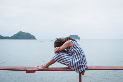 Woman sitting on railing by sea against sky