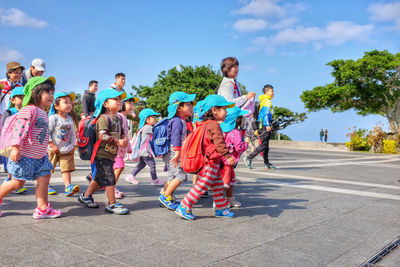 People with children walking on footpath against sky