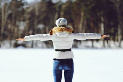 Rear view of woman with arms outstretched standing on snow