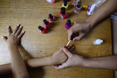 Overhead view of mother applying nail polish on daughter's fingernails at home