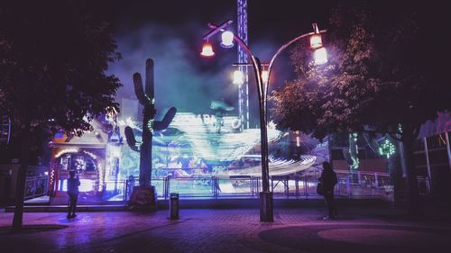 Illuminated street light in city against sky at night