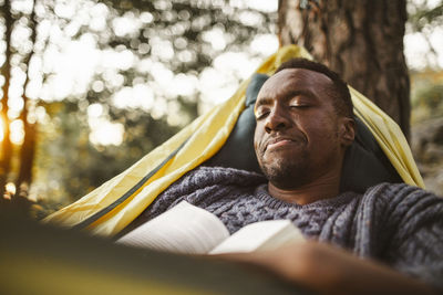 Man with book sleeping in hammock at forest