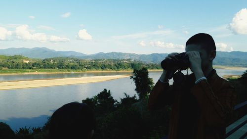 Rear view of woman photographing lake against sky