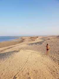 Rear view of woman standing on beach against clear sky